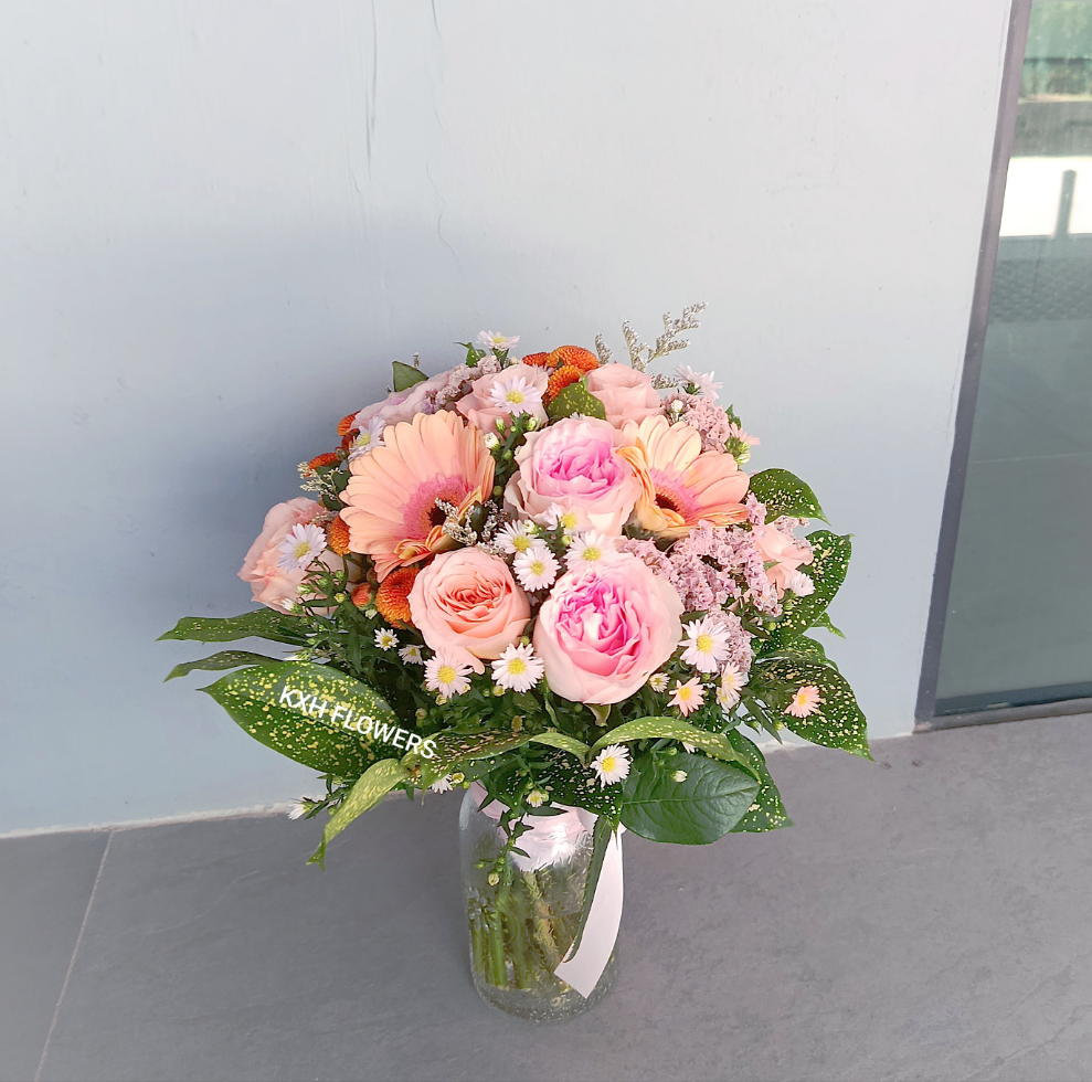 Hand-tied flower bunch in clear vase. Peach and pink roses, gerberas and mini daisies